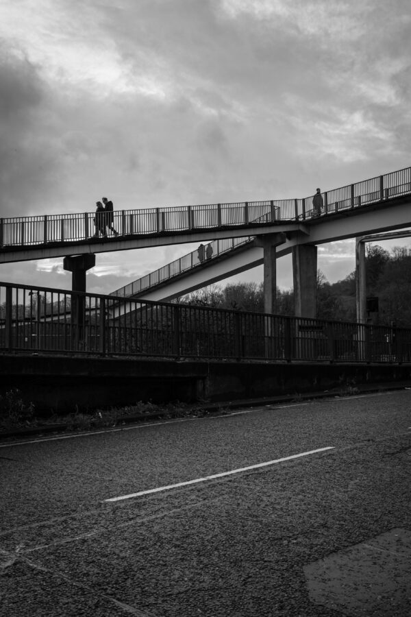 The footbridge across the Hotwell Road at the Cumberland Basin Flyover System in Hotwells, Bristol. Two couples and a third, single figure walk along three different sections of the bridge.
